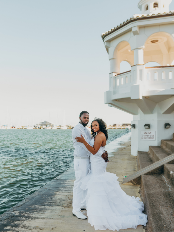 Everlasting Elopements couple holding each other looking at the camera standing by the ocean and in front of a gazebo at Miradores
